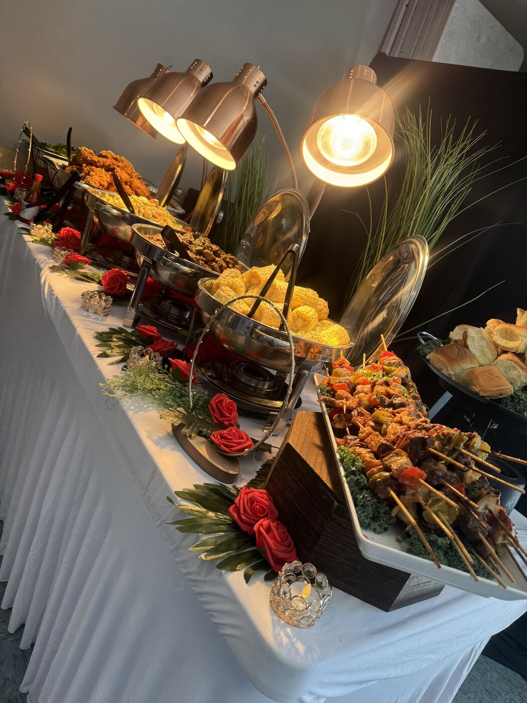 Catering buffet of skewers and fried chicken under heat lamps with roses